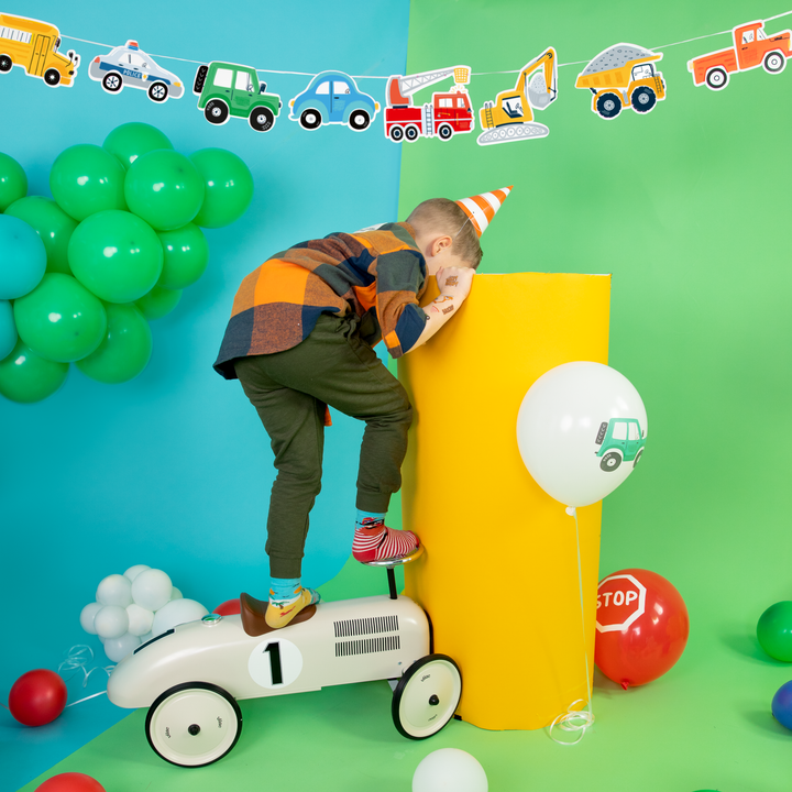 Zdjęcie aranżacyjne z chłopcem oraz girlandą, balonami lateksowymi i czapeczką imprezowa z kolekcji Auta