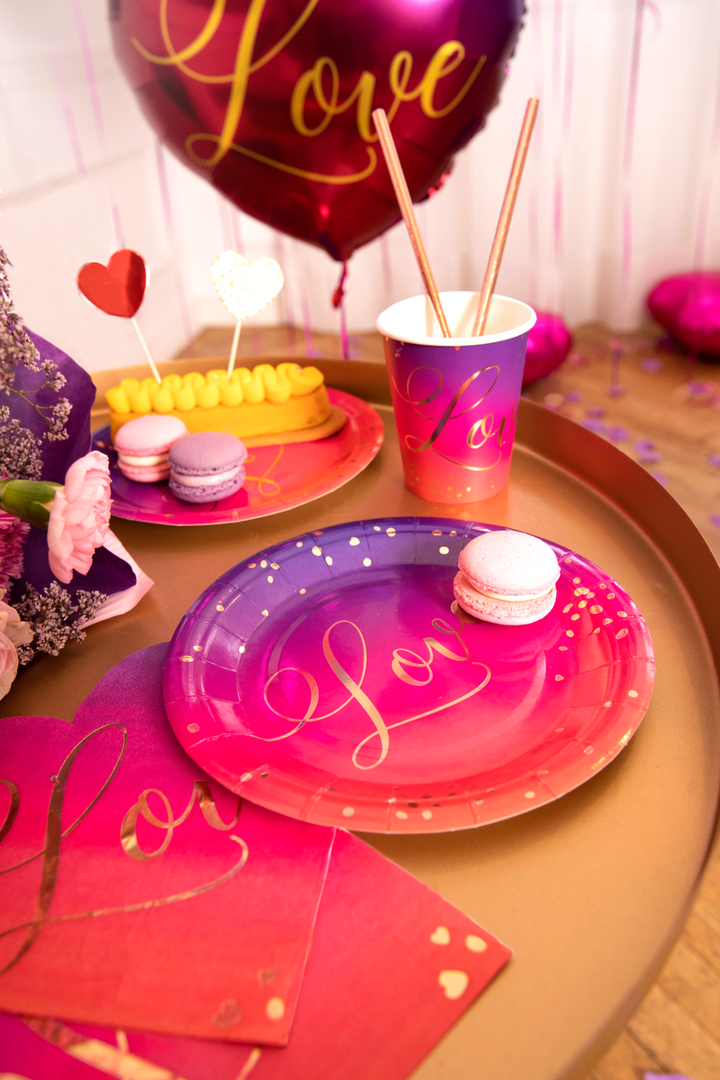 Kubek, talerzyki i serwetki z kolekcji Love na stoliku kawowym. W tle balon foliowy z napisem Love.