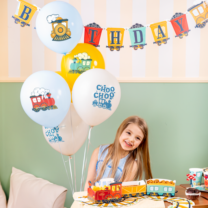 balony lateksowe z motywem ciuchci napisami choo choo, uśmiechnięta dziewczynka z długimi włosami, banner w kształcie pociągu, ciuchcią i wagonikami z węglem i napisem happy birthday, pudełka na chipsy w kształcie pociagu, serwetki z motywem torów kolejowych, kubeczki z motywem ciuchci