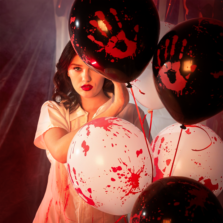 na pierwszym planie balony lateksowe białe i czarne z nadrukiem zakrwawionej dłoni i plam krwi z kolekcji bloody na halloween, za nimi stoi dziewczyna