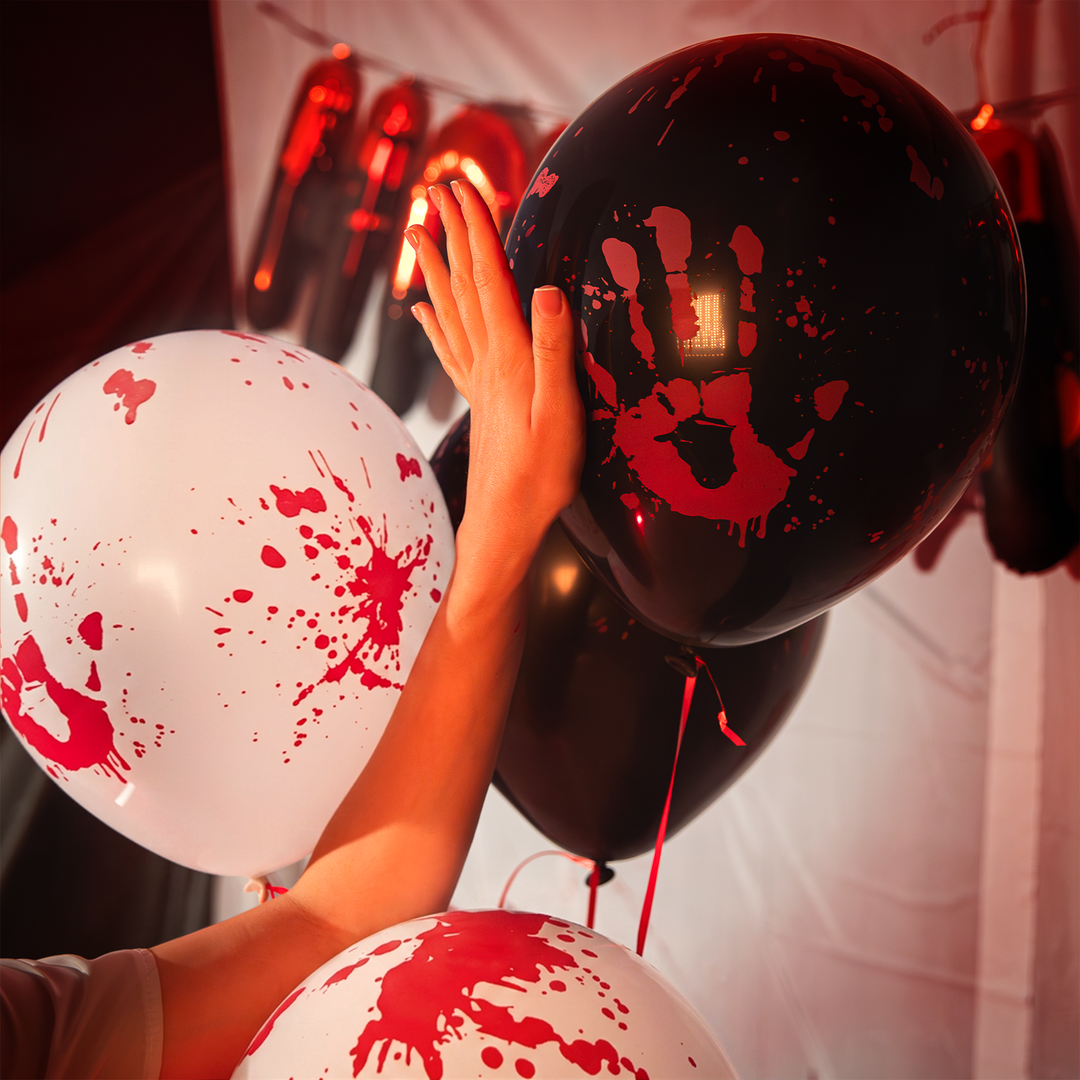 dłoń dziewczyny przykładana do balonów lateksowych białych i czarnych z nadrukiem zakrwawionej dłoni i plam krwi z kolekcji bloody na halloween