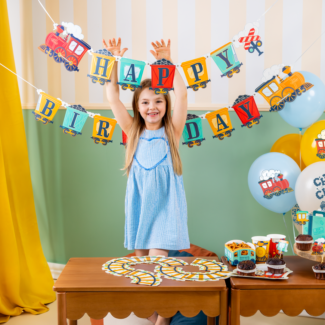 pokój  udekorowany banerem z motywem ciuchci i wagoników z napisem Happy Birthday, balony lateksowe z ciuchcią i napisem choo choo, na stole serwetki w kształcie torów kolejowych, kubeczki, pudełka na chipsy, toppery z motywm ciuchci, radosna dziewczynka