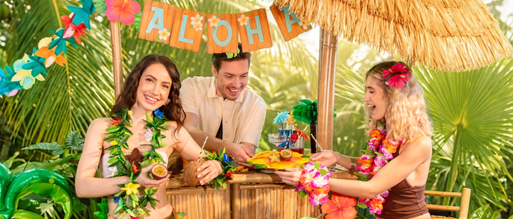 baner z napisem aloha z kolorywymi kwiatami hawajskimi, girlanda z hawajskimi kwiatami i liśćmi, egzotyczne owoce, ludzie śmiejący się, koktajle, talerzyki w kształcie kwiatów hawajskich, kokos, palma, bar, parasol, zabawa, fun, honeycomb papierowy ananas
