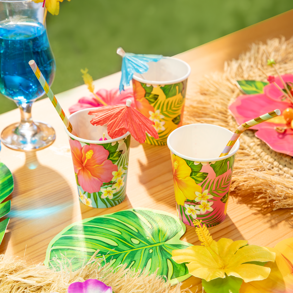 kubki papierowe aloha z motywem tropikalnych kwiatów w kolorze żółtym, różowym i pomarańczowym, parasolki koktajlowe, napoje, drinki, koktajle, serwetki w kształcie liści, słomki papierowe, tropikalne kwiaty
