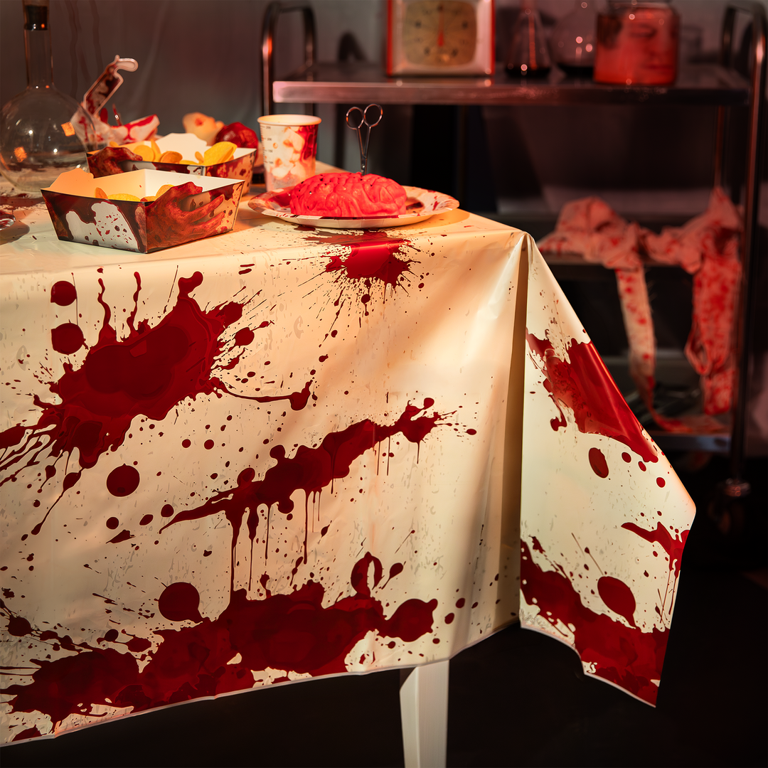 obrus plastikowy w plamy krwi na halloween. Na stole pudełko na chipsy, kubek papierowy jednorazowy, talerz papierowy jednorazowy, wszystkie dekoracje z motywem krwi z kolekcji bloody na halloween