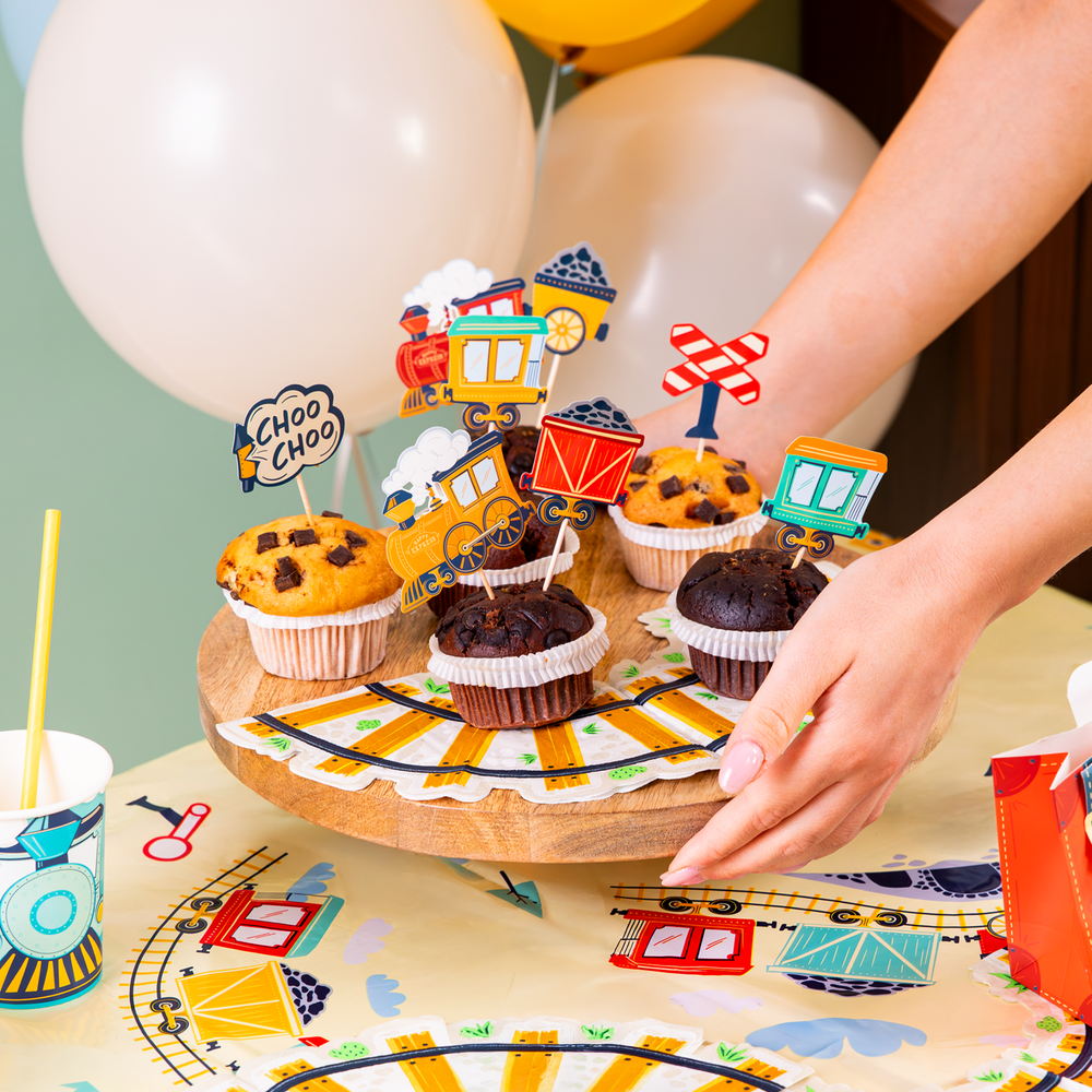 babeczki udekorowane topperami z motywem kolejowym, pociągów z kolekcji ciuchcia, w tle balony lateksowe, na stole obrus 