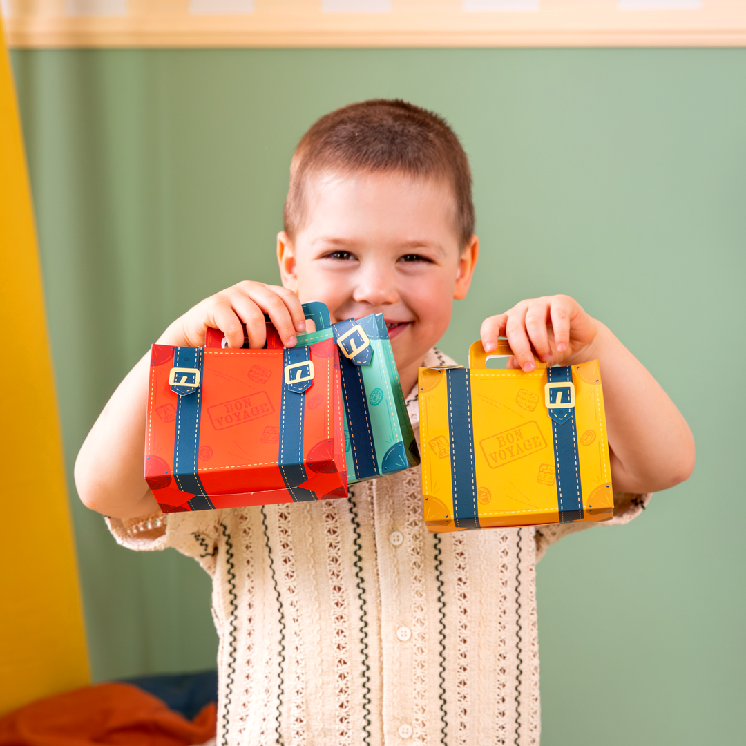Uśmiechnięty chłopiec trzymający w rączkach 3 torebki na cukierki z kolekcji ciuchcia, w kształcie walizek