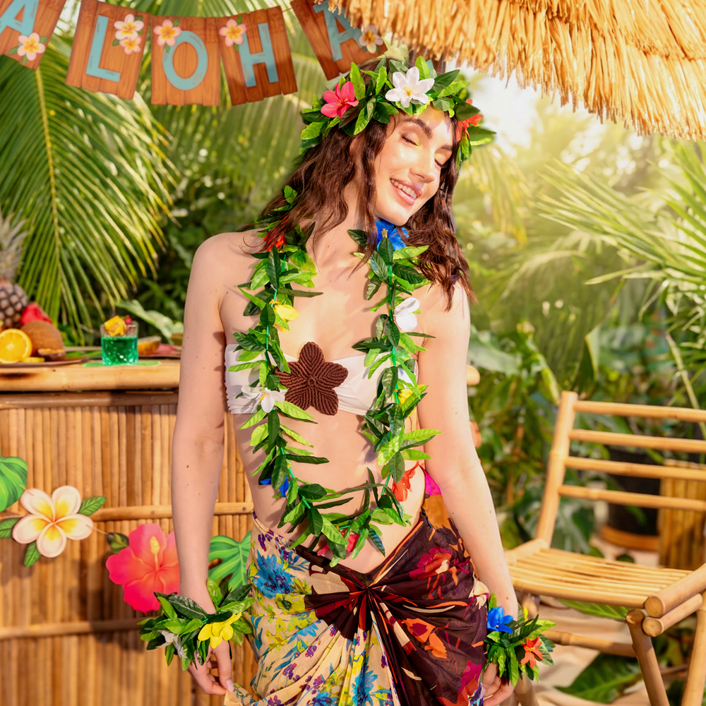 dziewczyna brunetka w zestawie hawajskim, naszyjniku, opasce i bransoletkach, bar, koktajle, baner aloha, parasol bambusowy, palmy, girlanda, parasolki koktajlowe