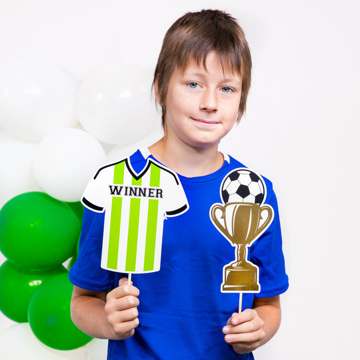 Chłopiec z dwoma rekwizytami fotograficznymi z kolekcji Football - koszulką z napisem Winner i pucharem z piłką.