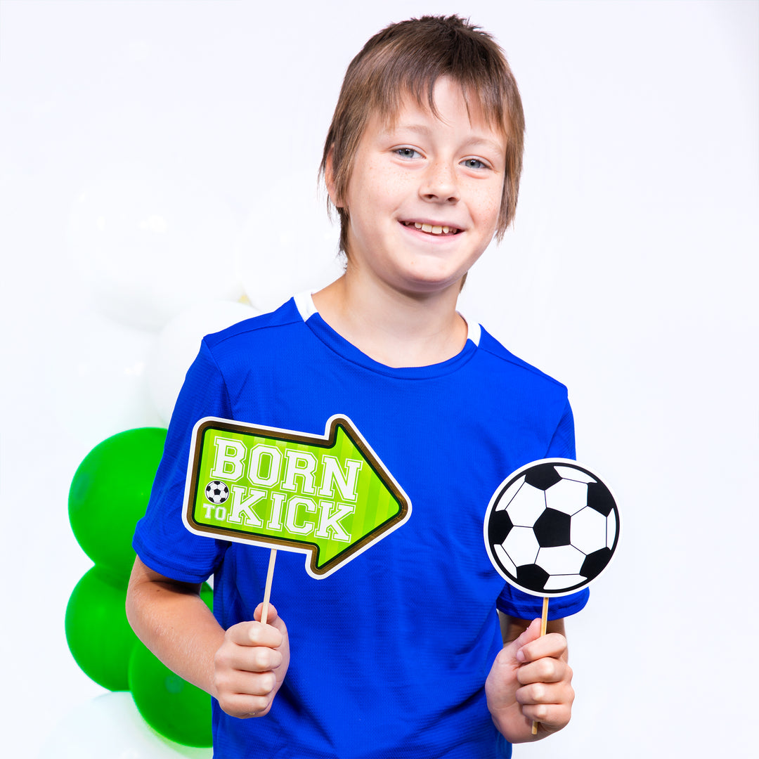 Uśmiechnięty chłopiec z dwoma rekwizytami fotograficznymi z kolekcji Football - tabliczką z napisem Born to kick i piłką