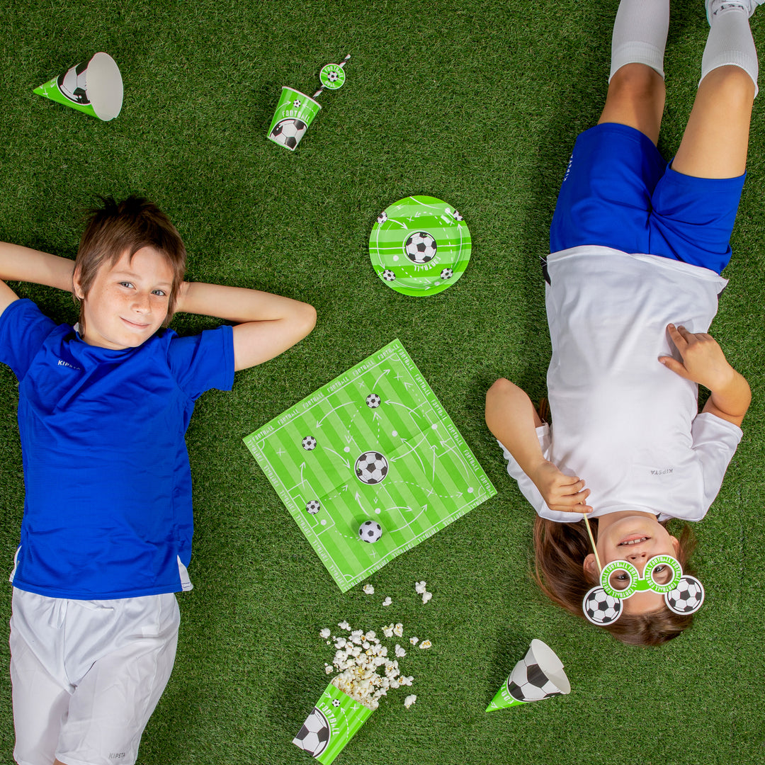 Dzieci leżące na zielonym dywanie z produktami z kolekcji Football  z centralnie ułożoną serwetka.