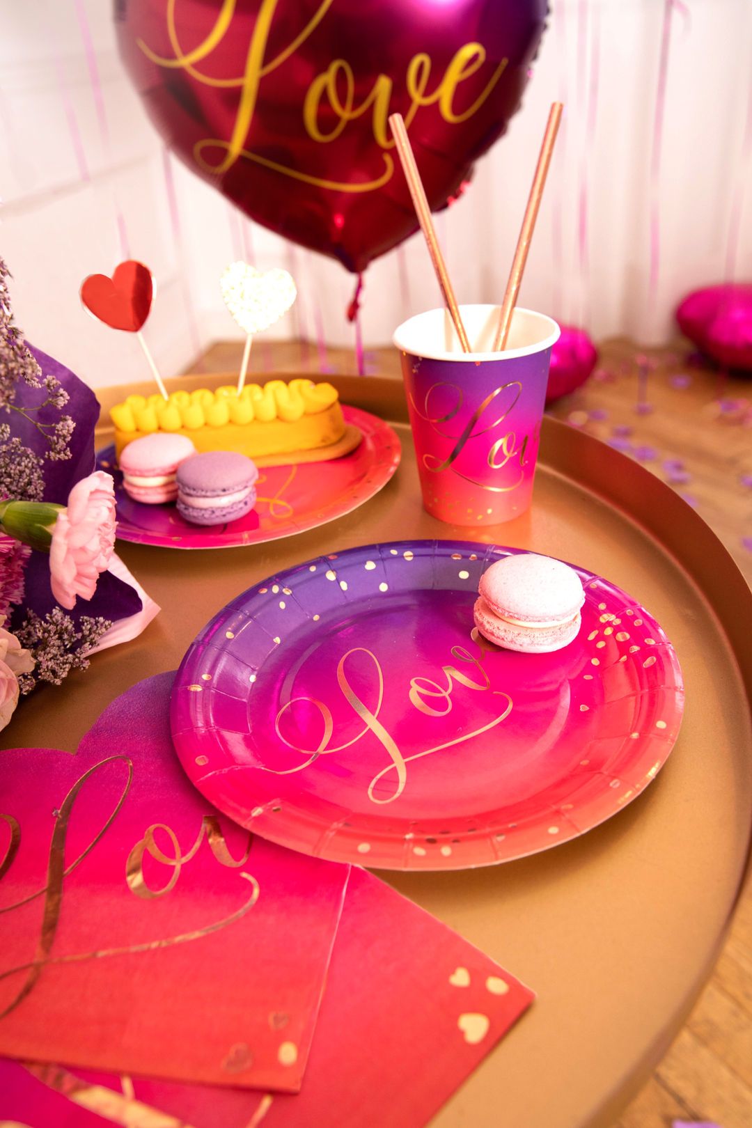 Kubek, talerzyki i serwetki z kolekcji Love na stoliku kawowym. W tle balon foliowy z napisem Love.