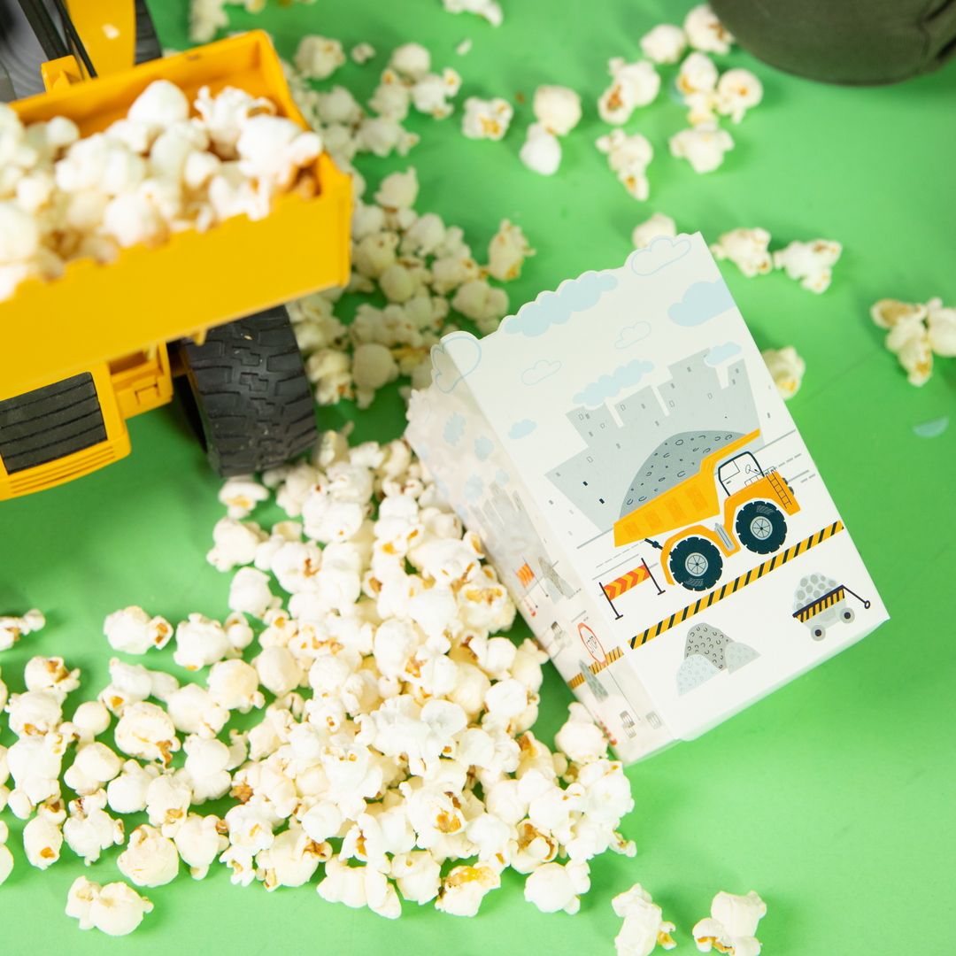 Pudełko na popcorn z ciężarówką na tle rozsypanego popcornu i koparki-zabawki