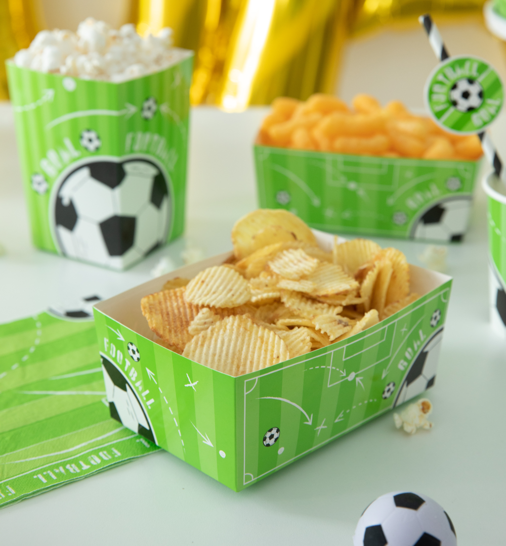 Na pierwszym planie znajduje się pudełko wypełnione chipsami stojące na serwetce z kolekcji Football.