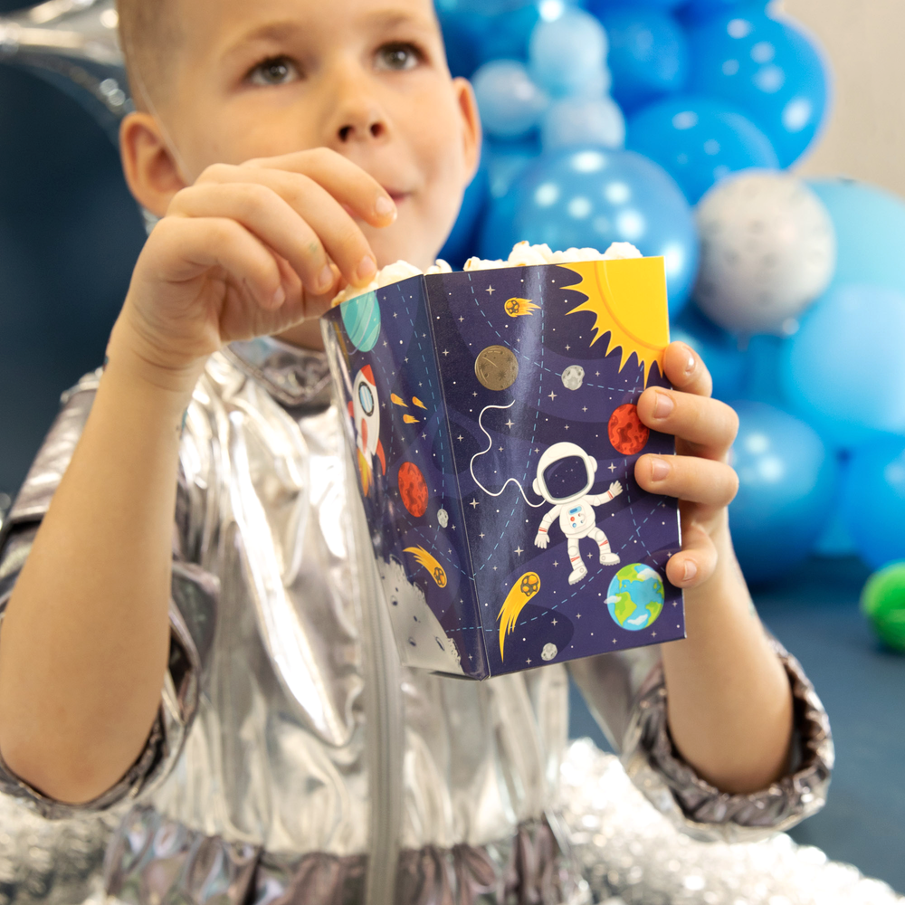 Chłopiec trzyma w ręku pudełko na popcorn  z kolorowymi grafikami Układu Słonecznego
