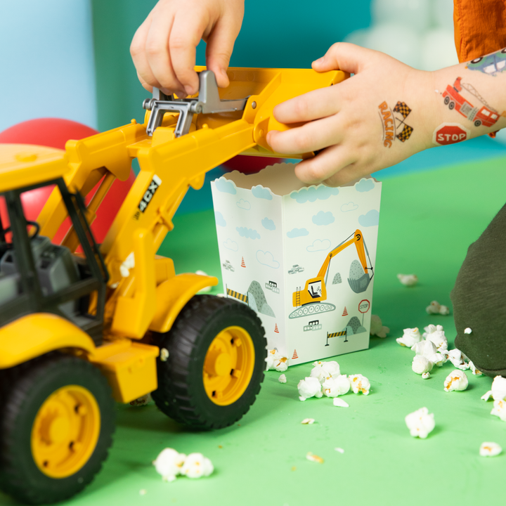 Dziecko bawi się małą koparką, wsypując popcorn do pudełka na popcorn z kolekcji Auta