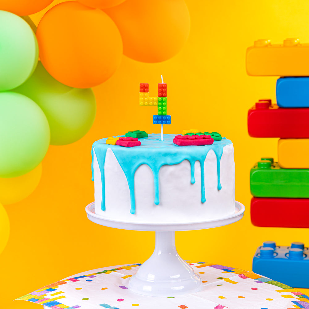 Świeczka na tort cyfra 4 w kolorowym otoczeniu balonów, klocków i tortu.
