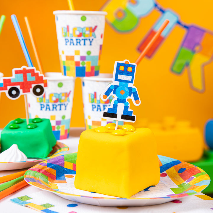 Topper z grafiką robota z klocków, wbity w ciastko przypominające żółty klocek lego.