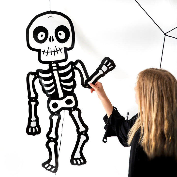 Dziewczynka trzyma za rękę wiszący na białej ścianie szkielet Halloween Monsters